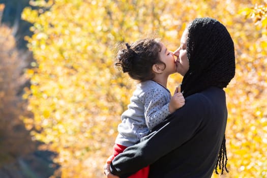 Autumn season nature scene with young mother and a little girl in her hug, Muslim family having fun in outdoor area
