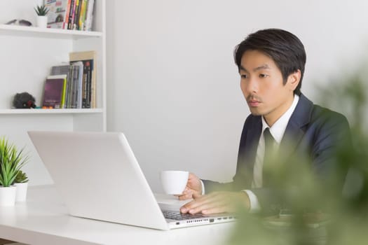 Asian Businessman with White Coffee Cup in Break Time with Tree Foreground in Office. Relax time for Asian businessman