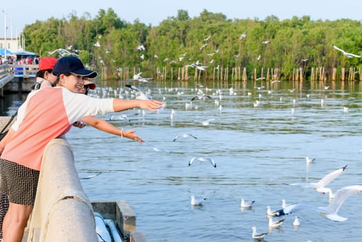 Woman and girl Asian family tourist, mother and daughter are happy fun feeding the seagulls flying above the sea, Travel Asia at Bangpu Recreation Center, Famous attraction of Samut Prakan, Thailand