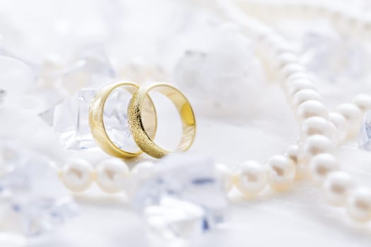 Two golden rings with pearl necklace and on white background as symbol of love and marriage
