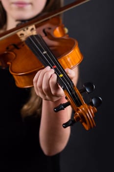 Close up of professional violin in hands of little girl playing it on black background
