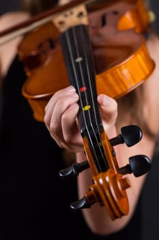 Close up of professional violin in hands of little girl playing it on black background