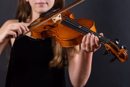 Close up of professional violin in hands of little girl playing it on black background