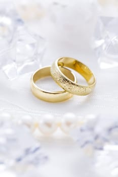 Two golden rings with pearl necklace and on white background as symbol of love and marriage