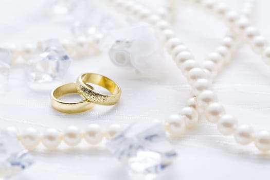 Two golden rings with pearl necklace and on white background as symbol of love and marriage