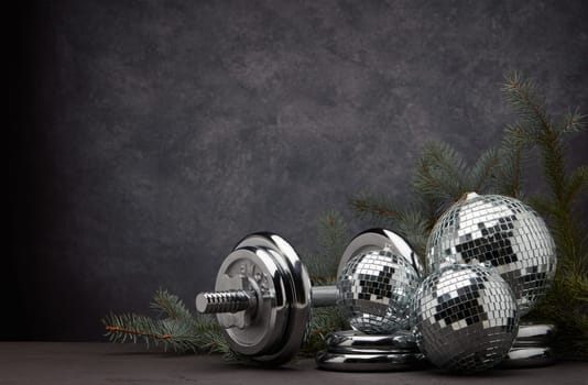 Sports equipment (dumbbell with weights), fir branch, Christmas ornament on dark grey background with copy space. Fitness, sport or healthy lifestyle concept. New Year and Christmas.