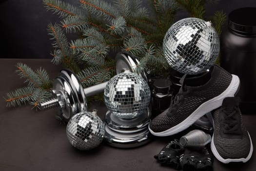 Sports nutrition (supplements), sports equipment, branch of fir, Christmas ornaments on dark grey background. Fitness, sport or healthy lifestyle concept. New Year and Christmas.