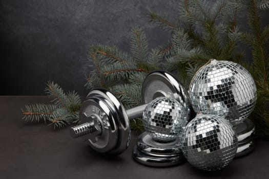 Sports equipment (dumbbell with weights), fir branch, Christmas ornament on dark grey background. Fitness, sport or healthy lifestyle concept. New Year and Christmas.