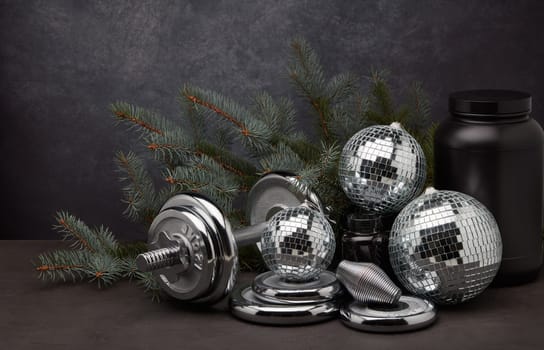 Sports nutrition (supplements), sports equipment, branch of fir, Christmas ornaments on dark grey background. Fitness, sport or healthy lifestyle concept. New Year and Christmas.