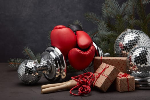 Sports equipment: dumbbell, boxing gloves, skipping rope, fir branch, Christmas ornament, gifts on dark grey background. Fitness, sport, healthy lifestyle concept. New Year. Christmas