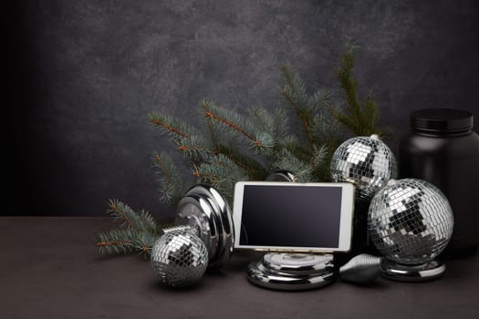 Sports nutrition, sports equipment, fir branch, Christmas ornament, blank computer tablet on dark grey background with copy space. Fitness, sport or healthy lifestyle concept. New Year and Christmas.