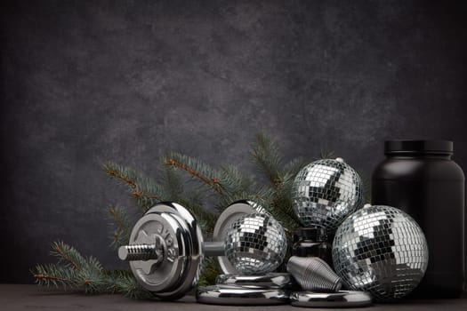 Sports nutrition (supplements), sports equipment, branch of fir, Christmas ornaments on dark grey background with copy space. Fitness, sport or healthy lifestyle concept. New Year and Christmas.