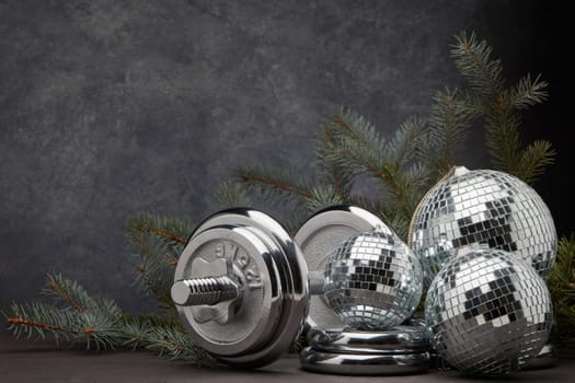 Sports equipment (dumbbell with weights), fir branch, Christmas ornament on dark grey background with copy space. Fitness, sport or healthy lifestyle concept. New Year and Christmas.