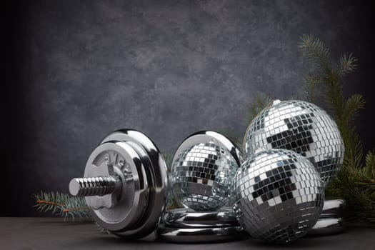 Sports equipment (dumbbell with weights), fir branch, Christmas ornament on dark grey background with copy space. Fitness, sport or healthy lifestyle concept. New Year and Christmas.
