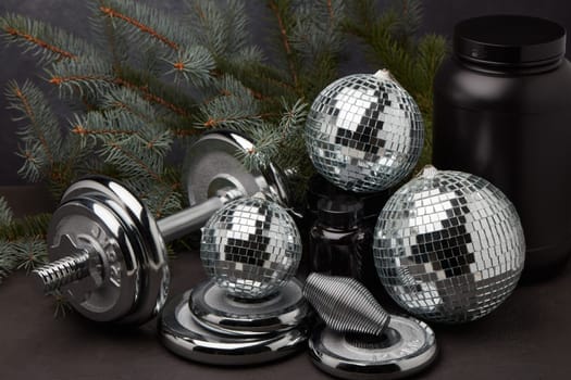 Sports nutrition (supplements), sports equipment, branch of fir, Christmas ornaments on dark grey background. Fitness, sport or healthy lifestyle concept. New Year and Christmas.