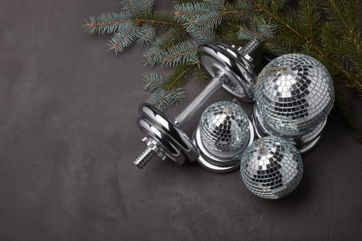 Sports equipment (dumbbell with weights), fir branch, Christmas ornament on dark grey background. Top view with copy space. Fitness, sport or healthy lifestyle concept. New Year and Christmas.