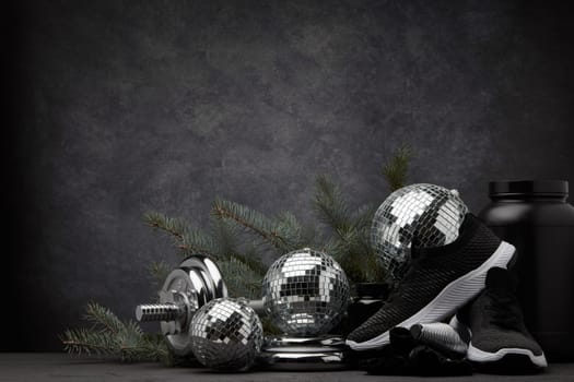 Sports nutrition (supplements), sports equipment, branch of fir, Christmas ornaments on dark grey background with copy space. Fitness, sport or healthy lifestyle concept. New Year and Christmas.