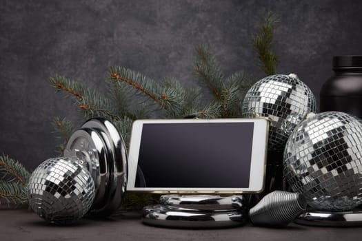 Sports nutrition, sports equipment, fir branch, Christmas ornament, blank computer tablet on dark grey background. Fitness, sport or healthy lifestyle concept. New Year and Christmas.