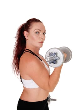 A middle age woman standing in profile lifting her dumbbells.whit her long red hair and workout outfit, isolated for white background.