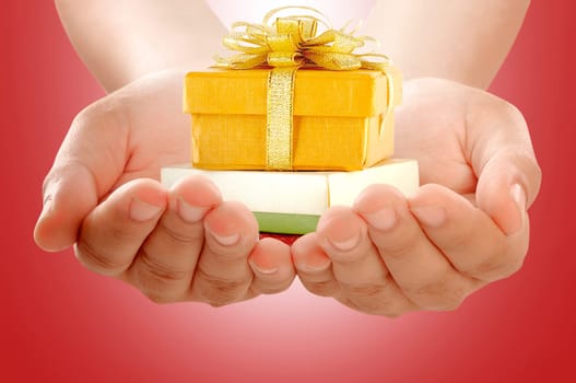 Hands holding colorful gift box with ribbon over red background