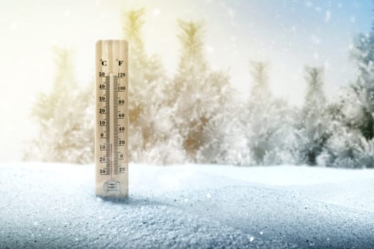 Wooden thermometer with the low temperature at winter with snowfall background