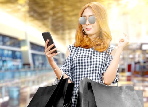 Asian woman using the mobile phone while holding black shopping bags in the mall. Black Friday concept
