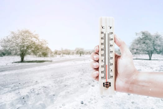 Hand holding thermometer measuring the temperature outdoor with a clear sky background. Heatwave concept