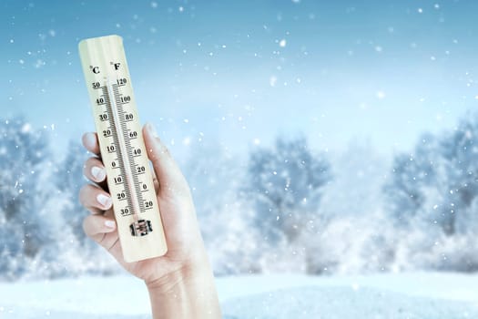 Hand holding wooden thermometer with the low temperature at winter with snowfall background