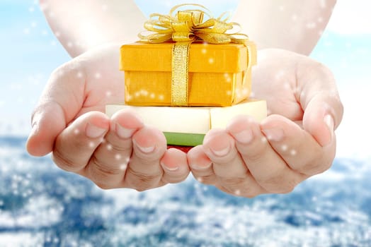 Hands holding colorful gift box with ribbon over snowy background