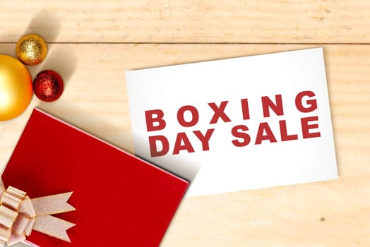 Gift box with a ribbon and Christmas ornament with Boxing Day Sale text on paper with wooden table background