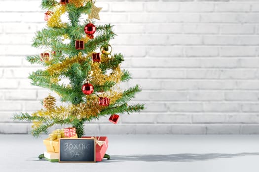 Christmas tree with gift box and Boxing Day text on the blackboard over brick wall background