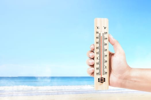 Hand holding thermometer measuring the temperature on the beach with a blue sky background. Heatwave concept
