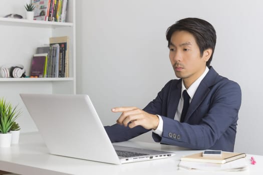 Asian Financial Advisor or Asian Consulting Businessman in Suit Recommend Customer Via Internet in Office. Asian financial advisor or Asian consulting businessman pointing laptop monitor