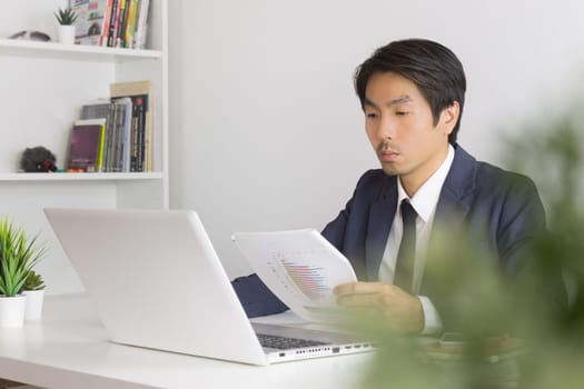 Asian Financial Advisor or Asian Consulting Businessman Analyze Financial Report in front of Laptop. Asian financial advisor or Asian consulting businessman working in office
