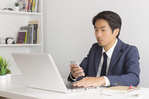 Asian Financial Advisor or Asian Consulting Businessman Sending Message or Chat with Customer. Asian Financial Advisor or Asian Consulting Businessman use smartphone in office