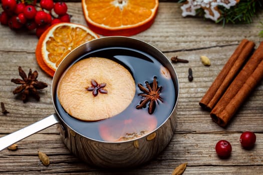 Small stewpot with mulled wine and cinnamon sticks, slice of oranges and apple on wooden table top view. Hot winter drink. Christmas beverage.