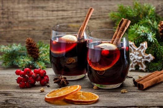 Mulled wine in glasses in a Christmas setting with dry slices of oranges, cookies in the shape of a snowflake, red berries and cinnamon
