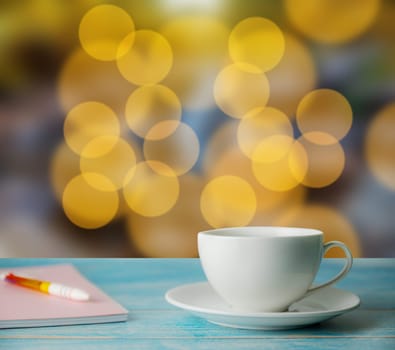 A cup of coffee and notebook with abstract bokeh street light background, Christmas light bokeh and light bulbs blurred background