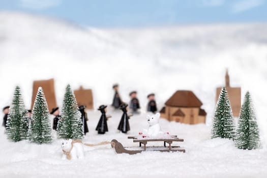 Christmas greeting card template. Focus on polar bear pulls a sleigh with another bear on it through the snow against blurred toy trees, wooden figures, houses and snowy mountains. Space.