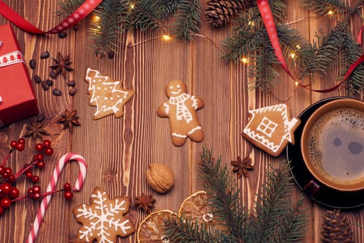 Christmas decor with fir tree branches, gingerbreads and gift box on a wooden background with copy space for text. Top view. For greeting card.