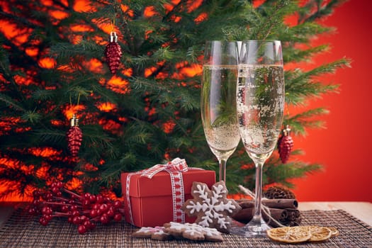 Two glasses with champange, fir tree, gift boxes and christmas ginger cookies on a red background. New year and Christmas.