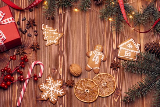 Christmas decor with fir tree branches, gingerbreads and gift box on a wooden background with copy space for text. Top view. For greeting card.