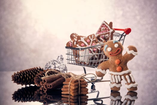 Shopping trolley with gingerbread cookies and christmas decorations standing on a grey background with reflection. Christmas and New Year sale.
