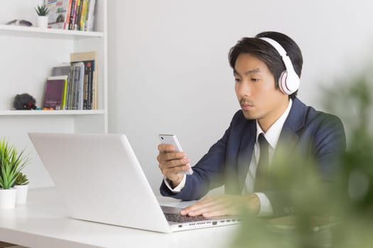 Asian Man Call Center Contact with Customer by Smartphone and Laptop. Asian man call center answers the customer question in front of laptop in office