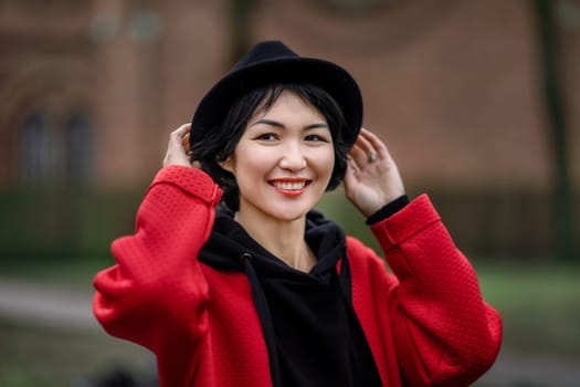Oriental girl in a red stylish coat and black hat in an urban environment