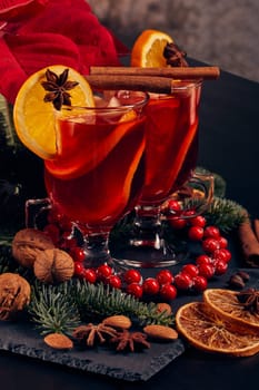 Still life with glasses of mulled wine or fruit tea, Red Poinsettia flowers, fir branch and spices on a dark background. New year and Christmas table setting. Greeting card.