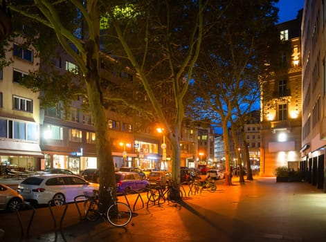 Evening street scene, illuminated downtown with parked cars and bicycles, platan trees, cafes and shops, Frankfurt am Main, Germany