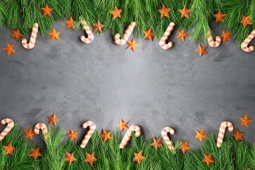 Christmas border of pine boughs, rustic stars and wooden candy canes on slate surface, copy space in the middle.