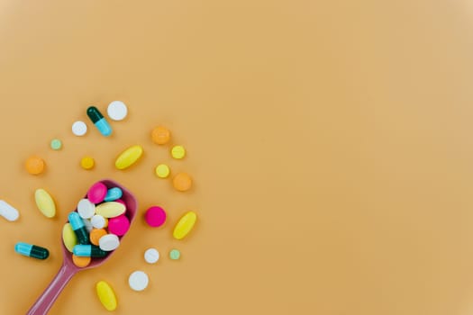 Assorted pharmaceutical medicine pills, tablets and capsules, and spoon on yellow background. Copy space for text, top view.