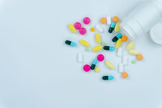 Assorted pharmaceutical medicine pills, tablets and capsules, and bottle on white background. Copy space for text, top view.
